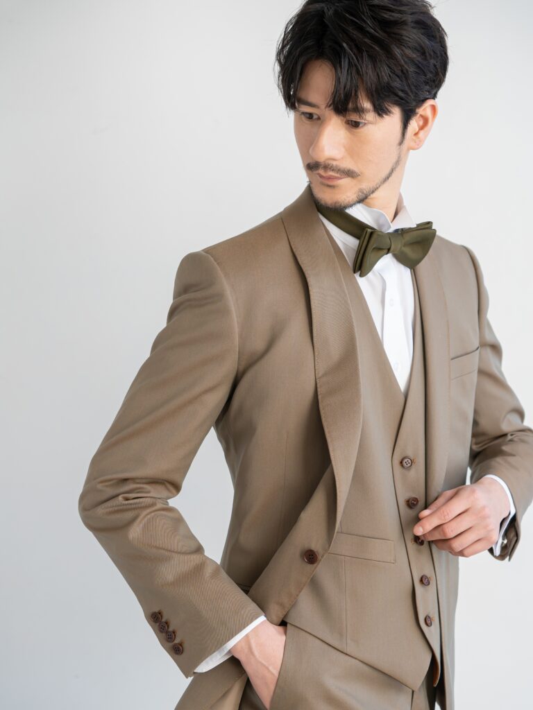 【AMM-023 カーキ】カーキ・オレンジの2色の糸を使った上品な光沢感が特徴の交織シャンブレー生地。絶妙な色目でどんな色のドレスとも相性が良く、マルチに活躍できるメンズタキシードです。テラコッタのリバーシブルベスト。ジャケットとの色合わせがおしゃれで、ガラッと雰囲気が変わるため、お色直しのシーンにも重宝するデザインになっています。