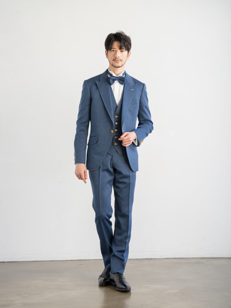 AMM-021(ネイビー)| 「ナチュレミア」という新素材を使ったデニムブルーのタキシード。デニムに見えますがデニムとは違い、 ポリエステル100%でありながら、天然素材のような肌触りと質感を持ち吸水性と速乾性、シワになりにくい強度を兼ね備えた大変扱いやすい生地で仕立てています。 手入れがしやすく、永く使うことができる世界的なSDG'sの潮流を汲んだ新素材です。 独特の色目で、カジュアルさの中にこだわりとおしゃれ要素が内包された ハイブリッドなデザインがご好評をいただいております。 また、ベージュのリバーシブルベストで印象を変えて、気軽におしゃれを楽しむようにお召しいただけます。