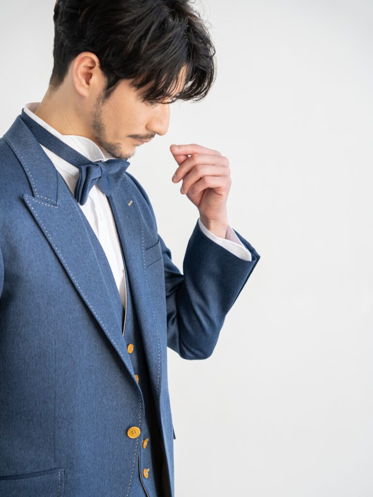 AMM-021(ネイビー)| 「ナチュレミア」という新素材を使ったデニムブルーのタキシード。デニムに見えますがデニムとは違い、 ポリエステル100%でありながら、天然素材のような肌触りと質感を持ち吸水性と速乾性、シワになりにくい強度を兼ね備えた大変扱いやすい生地で仕立てています。 手入れがしやすく、永く使うことができる世界的なSDG'sの潮流を汲んだ新素材です。 独特の色目で、カジュアルさの中にこだわりとおしゃれ要素が内包された ハイブリッドなデザインがご好評をいただいております。 また、ベージュのリバーシブルベストで印象を変えて、気軽におしゃれを楽しむようにお召しいただけます。