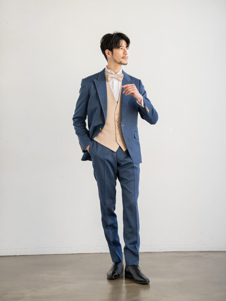 AMM-021(ネイビー)| 「ナチュレミア」という新素材を使ったデニムブルーのタキシード。デニムに見えますがデニムとは違い、 ポリエステル100%でありながら、天然素材のような肌触りと質感を持ち吸水性と速乾性、シワになりにくい強度を兼ね備えた大変扱いやすい生地で仕立てています。 手入れがしやすく、永く使うことができる世界的なSDG'sの潮流を汲んだ新素材です。 独特の色目で、カジュアルさの中にこだわりとおしゃれ要素が内包された ハイブリッドなデザインがご好評をいただいております。 また、ベージュのリバーシブルベストで印象を変えて、気軽におしゃれを楽しむようにお召しいただけます。