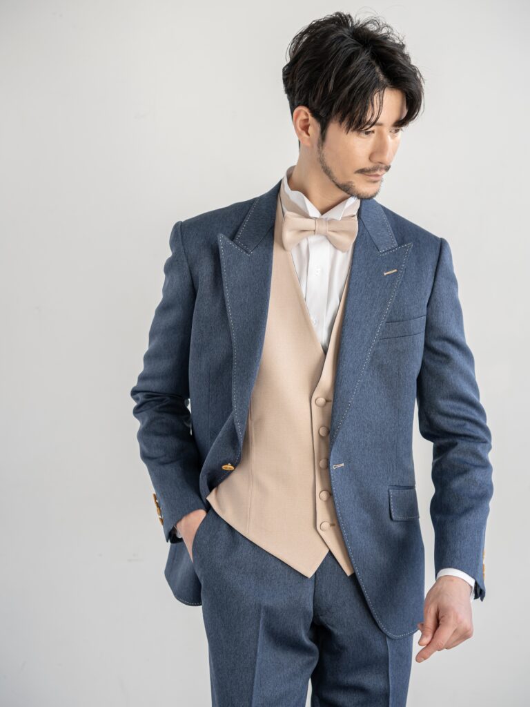 AMM-021(ネイビー)| 「ナチュレミア」という新素材を使ったデニムブルーのタキシード。デニムに見えますがデニムとは違い、 ポリエステル100%でありながら、天然素材のような肌触りと質感を持ち吸水性と速乾性、シワになりにくい強度を兼ね備えた大変扱いやすい生地で仕立てています。 手入れがしやすく、永く使うことができる世界的なSDG'sの潮流を汲んだ新素材です。 独特の色目で、カジュアルさの中にこだわりとおしゃれ要素が内包された ハイブリッドなデザインがご好評をいただいております。 また、ベージュのリバーシブルベストで印象を変えて、気軽におしゃれを楽しむようにお召しいただけます。