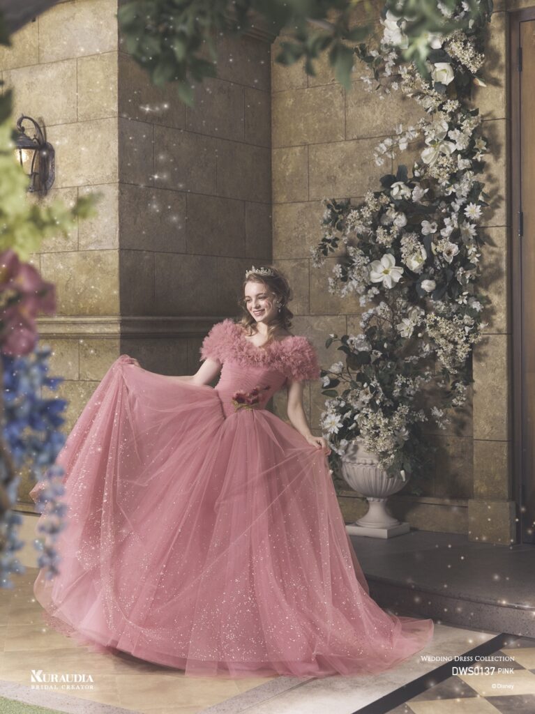 DWS0137 Pink 「Princess Aurora」| 「オーロラ姫」からインスパイアされたエレガントで女性らしいローズピンクのチュールドレスです。肩にのるフリルケープや、 ローズをイメージしたスパンコールのモチーフがポイントです。ローウエストのV字切り替えでシルエットをより美しく演出し、スカートには魔法がかかったようなグリッターが煌めき、上品な印象に。※ケープは取り外し可能です。