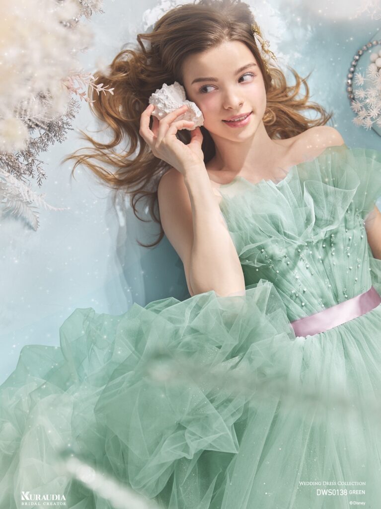 DWS0138 Blue Green 「Ariel」| 波のゆらめきを表現したタッキングのスカートがポイントの、「アリエル」からインスパイアされたボリュームドレスです。 ブルーグリーンの美しいグラデーションと、パープルのウエストリボンが「アリエル」らしいカラーリングです。バルーンデザインの裾やタッキングのスカートの内側からは海の中の光をイメージしたグリッターが光輝きます。動きのある立ち上がったドレープ身頃には海の泡を表現したパールやビーズがあしらわれています。
