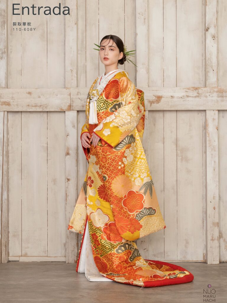 色打掛 110-608Y | 裂取という直線的な形で地を様々な文様、色に分け、その上に意匠化した梅や菊をあしらいました。梅は新春に寒さに先駆けて咲くことから春を告げる花とされており、菊は長寿の意味をもち、古くより愛されています。地には和が重なり、広がる様から別名「和繋ぎ文」と言われ永遠をあらわす七宝、亀の甲羅をデザインした亀甲といった吉祥文様をあしらい、織物にはめずらしくも染分けのように様々な色をあしらい晴れの日を彩るにぴったりの一枚が完成しました。