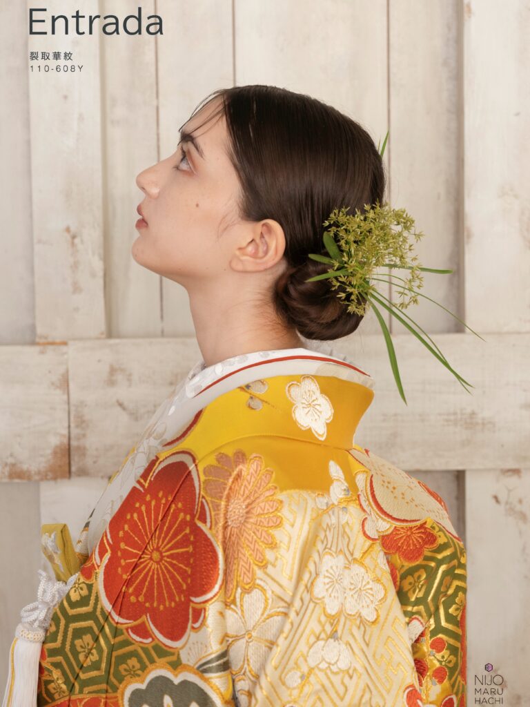 色打掛 110-608Y | 裂取という直線的な形で地を様々な文様、色に分け、その上に意匠化した梅や菊をあしらいました。梅は新春に寒さに先駆けて咲くことから春を告げる花とされており、菊は長寿の意味をもち、古くより愛されています。地には和が重なり、広がる様から別名「和繋ぎ文」と言われ永遠をあらわす七宝、亀の甲羅をデザインした亀甲といった吉祥文様をあしらい、織物にはめずらしくも染分けのように様々な色をあしらい晴れの日を彩るにぴったりの一枚が完成しました。