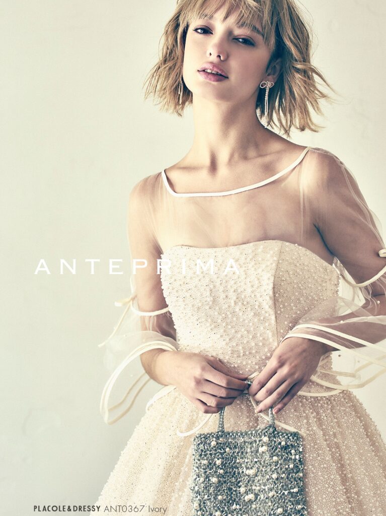 ANT0367(アイボリー/オレンジ) | ジュエルパールグリッターの輝きを全身にまとい、上品さと可憐さをあわせ持つ“現代のプリンセス”を表現。新素材“エアーファブリックオーガン”が、ふんわりと空気を含んだような軽やかなドレープを描きます。ピーチオレンジのやさしい色合いが肌にやわらかく映え、見る人にぬくもりと幸せを届けるような一着です。