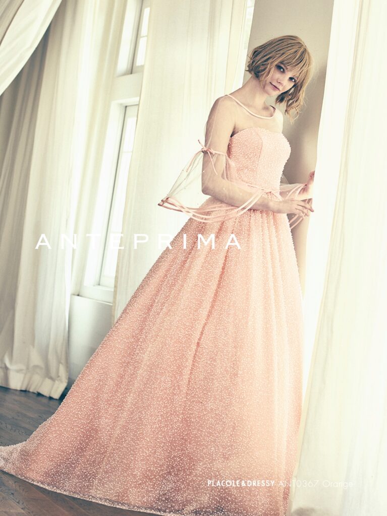 ANT0367(アイボリー/オレンジ) | ジュエルパールグリッターの輝きを全身にまとい、上品さと可憐さをあわせ持つ“現代のプリンセス”を表現。新素材“エアーファブリックオーガン”が、ふんわりと空気を含んだような軽やかなドレープを描きます。ピーチオレンジのやさしい色合いが肌にやわらかく映え、見る人にぬくもりと幸せを届けるような一着です。