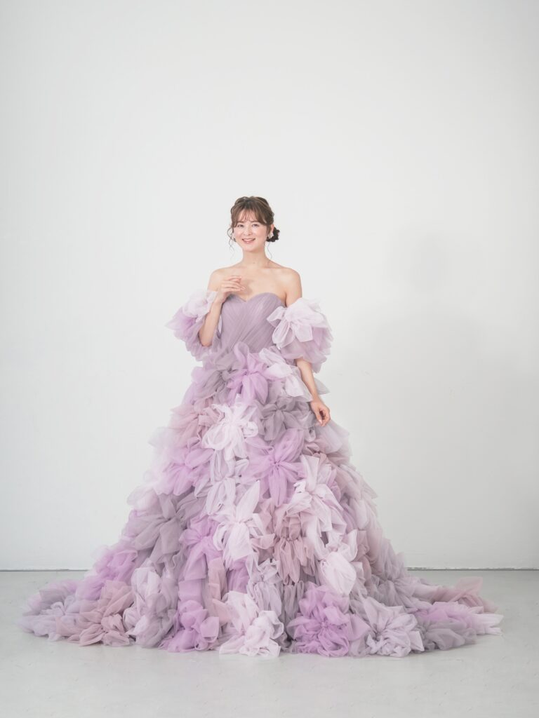 LQ-027(ラベンダー) | 柔らかいピンク・ラベンダーの色を複数混ぜ合わせてひとつずつふんわりと、立体的に形成したハンドメイドフラワーをそのまま身に纏うようなフォトジェニックなドレス。花びらを一枚一枚つまんでふんわり見せる工程や、お花中心のクリスタルをチュールでくるむ技法などよく見るととっても繊細な手仕事でできているのがわかります。