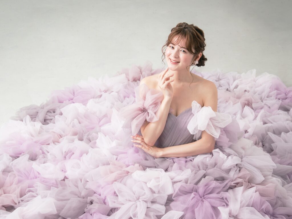 LQ-027(ラベンダー) | 柔らかいピンク・ラベンダーの色を複数混ぜ合わせてひとつずつふんわりと、立体的に形成したハンドメイドフラワーをそのまま身に纏うようなフォトジェニックなドレス。花びらを一枚一枚つまんでふんわり見せる工程や、お花中心のクリスタルをチュールでくるむ技法などよく見るととっても繊細な手仕事でできているのがわかります。