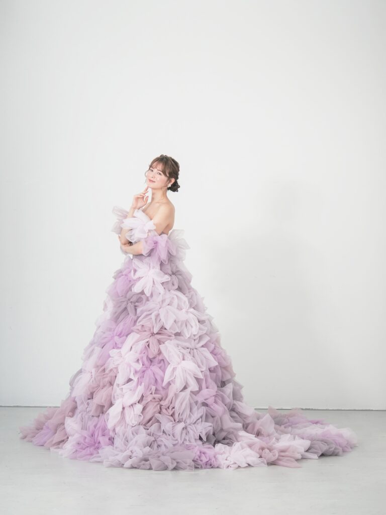 LQ-027(ラベンダー) | 柔らかいピンク・ラベンダーの色を複数混ぜ合わせてひとつずつふんわりと、立体的に形成したハンドメイドフラワーをそのまま身に纏うようなフォトジェニックなドレス。花びらを一枚一枚つまんでふんわり見せる工程や、お花中心のクリスタルをチュールでくるむ技法などよく見るととっても繊細な手仕事でできているのがわかります。