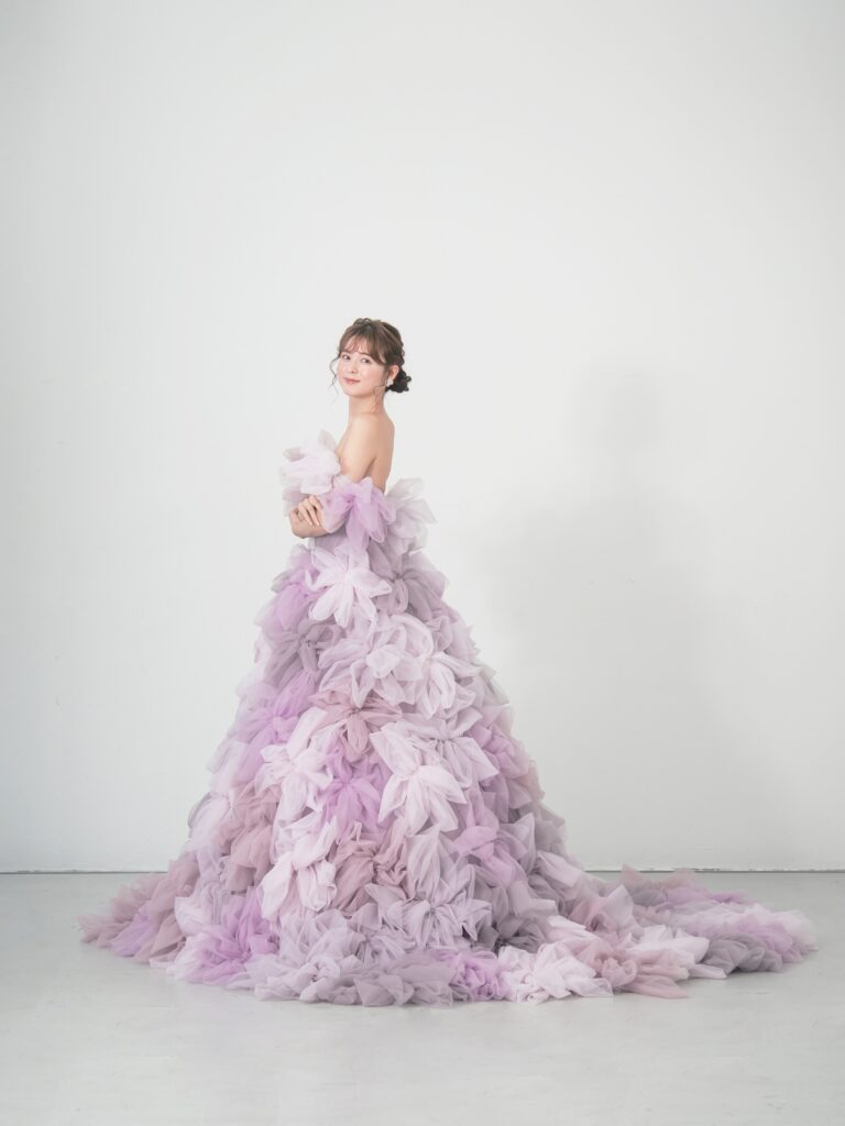 LQ-027(ラベンダー) | 柔らかいピンク・ラベンダーの色を複数混ぜ合わせてひとつずつふんわりと、立体的に形成したハンドメイドフラワーをそのまま身に纏うようなフォトジェニックなドレス。花びらを一枚一枚つまんでふんわり見せる工程や、お花中心のクリスタルをチュールでくるむ技法などよく見るととっても繊細な手仕事でできているのがわかります。