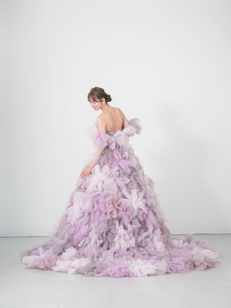 LQ-027(ラベンダー) | 柔らかいピンク・ラベンダーの色を複数混ぜ合わせてひとつずつふんわりと、立体的に形成したハンドメイドフラワーをそのまま身に纏うようなフォトジェニックなドレス。花びらを一枚一枚つまんでふんわり見せる工程や、お花中心のクリスタルをチュールでくるむ技法などよく見るととっても繊細な手仕事でできているのがわかります。