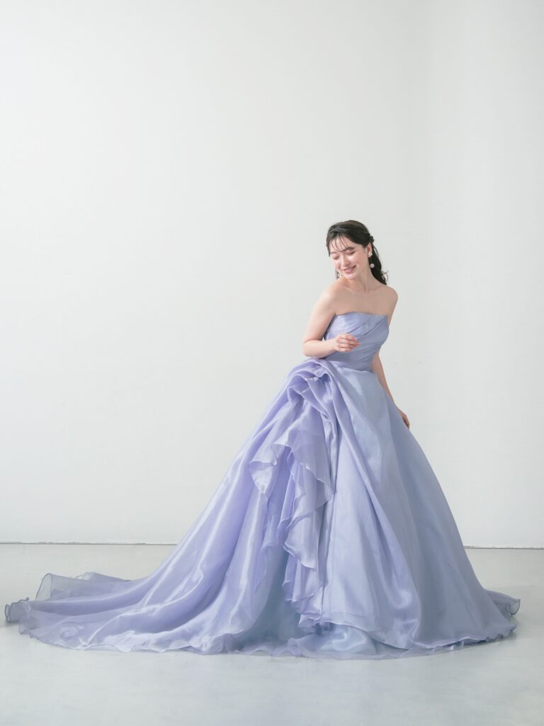 ST-111 | やわらかなウィスティリアカラーが空気まで優しく染める一着。透明感のあるオーガンジーの重なりと、流れるようなボリュームシルエットが、動くたびに表情を変えてくれます。 甘すぎず、上品で、記憶に残るカラードレス。静かな華やかさをまといたい花嫁さまへ。